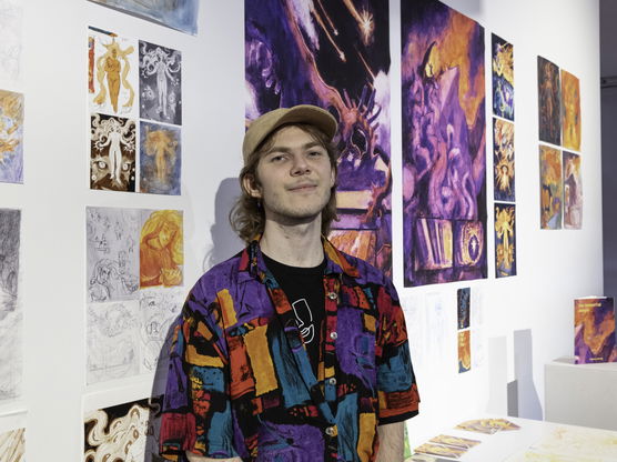 A PNCA BFA undergrad student wearing a colorful shirt in front of their work. 