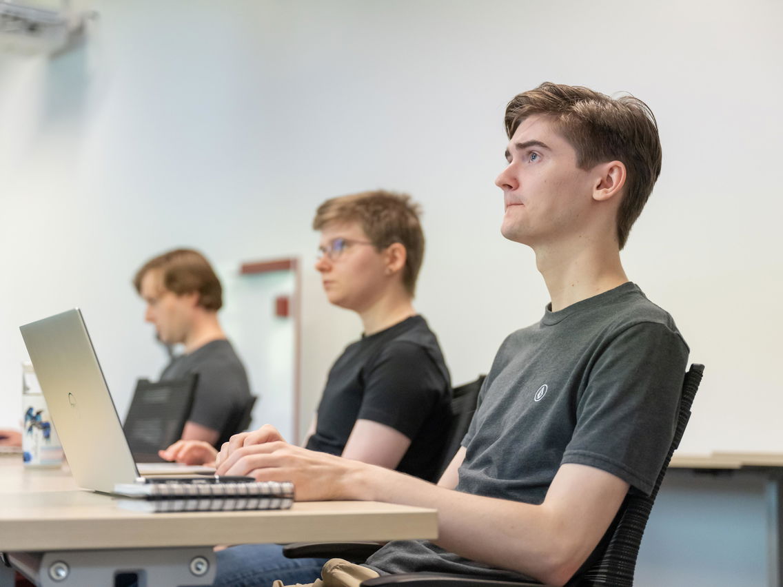 3 students sitting at a table in a classroom looking up. 