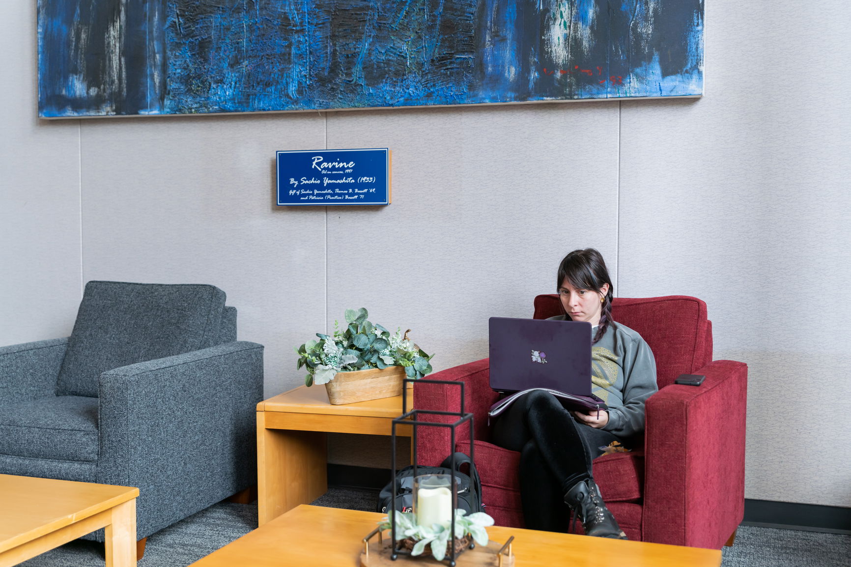 A student sitting on a red chair with their laptop