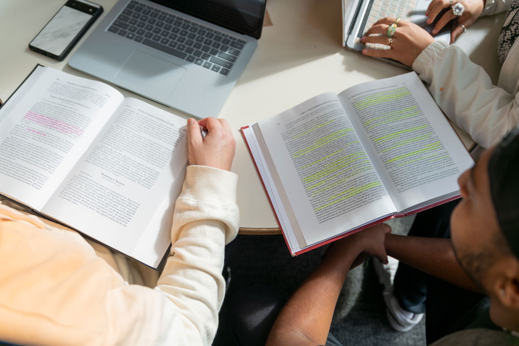 Close-up of a study session with two open books with highlighted text, a laptop, and a smartphone on a table.