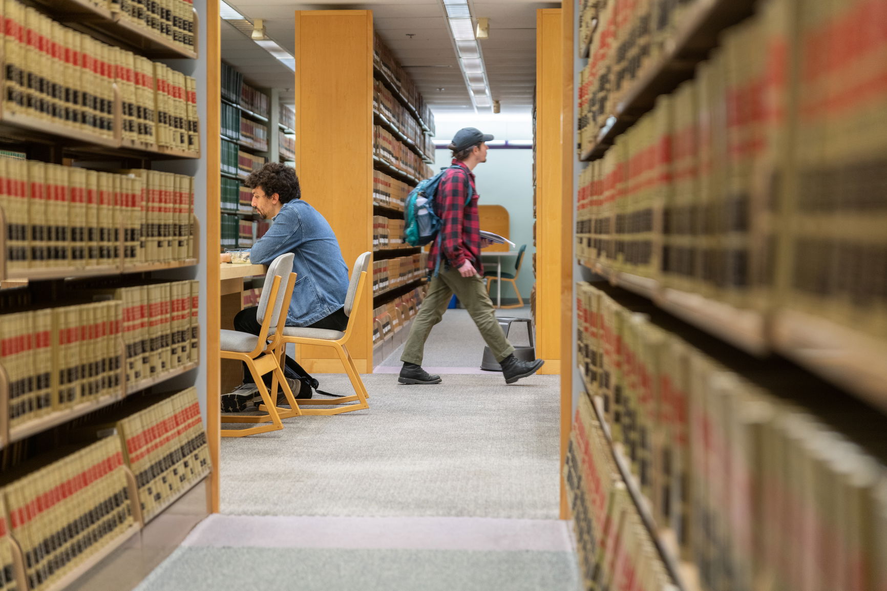 One student sitting and one student walking in the open area of a law library.