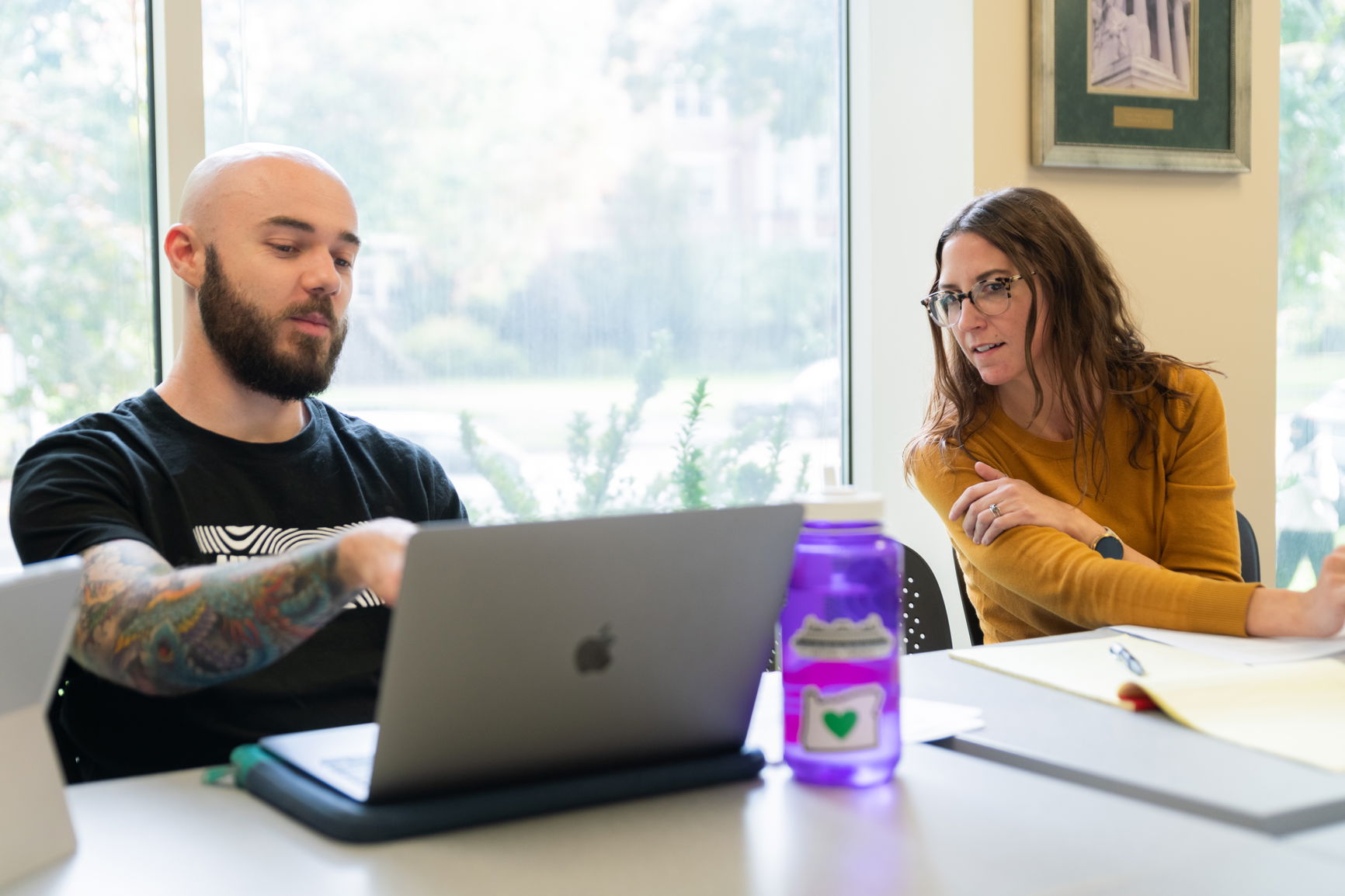 One student pointing at their laptop to show something to another student