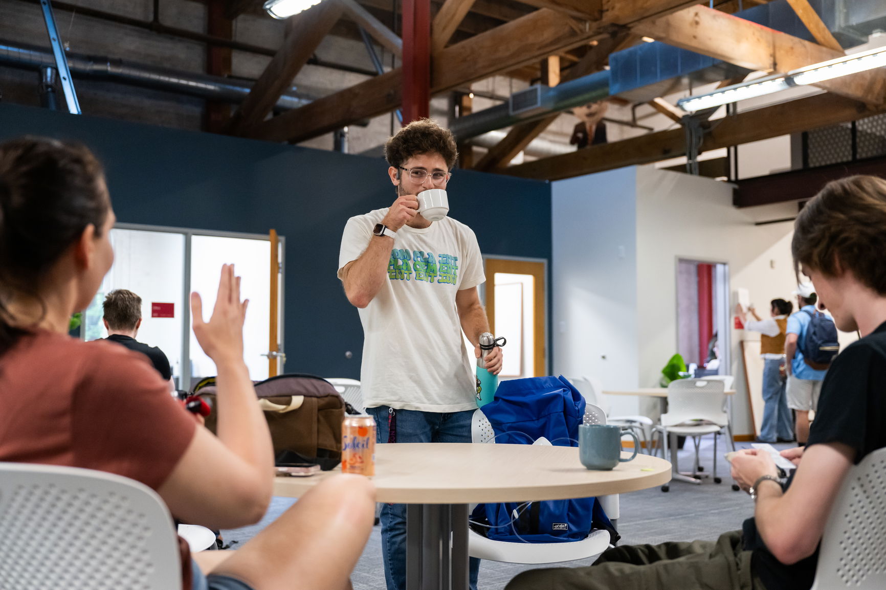 A guy sipping coffee and talking to two students at Willamette's Graduate and Professional Center