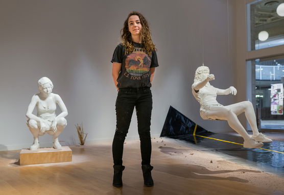 A person standing in front of human scultures, one squatting and one floating in the air.