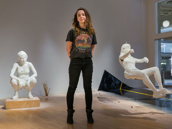 A person standing in front of human scultures, one squatting and one floating in the air.