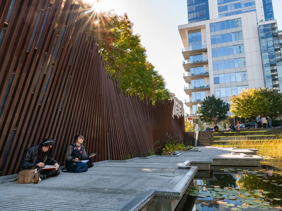 two people sit beside a large contemporary fence in a downtown city park