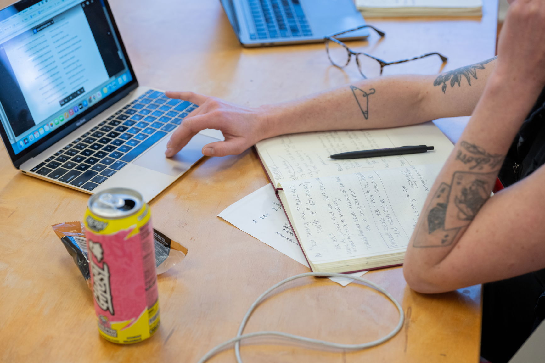 a photo of a person's hands writing in a binder with a laptop in front of them