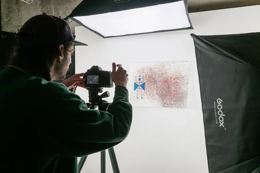 Person photographing an artwork with a camera under studio lighting.