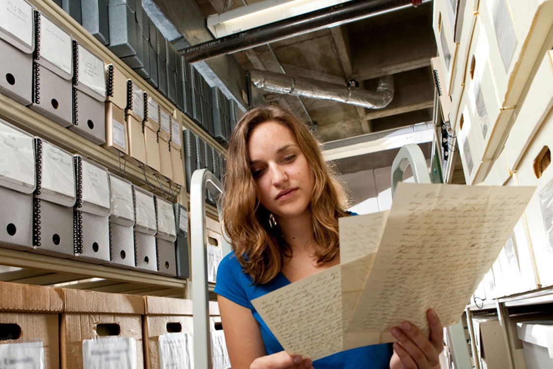 A student holding up papers in a library.