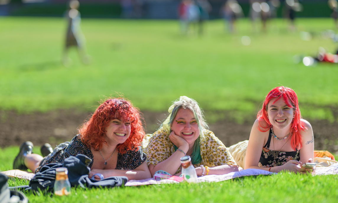 3 students with colorful hair laying in the quad. 