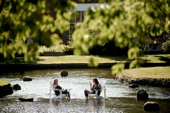 Two students sitting in white lawn chairs that are resting inside of Mill Stream on Willamette's Salem campus.