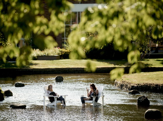 Two students sitting in white lawn chairs that are resting inside of Mill Stream on Willamette's Salem campus.