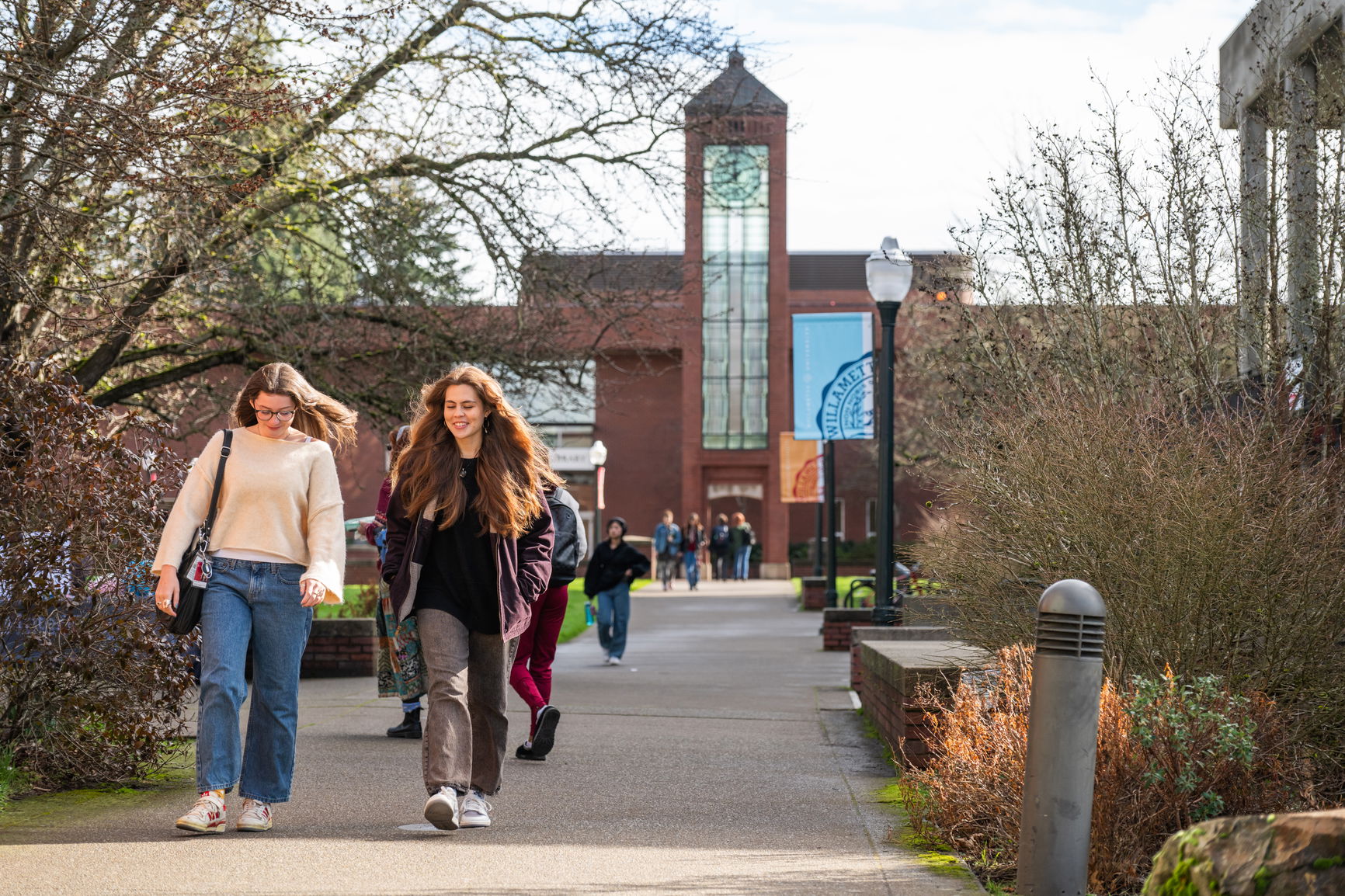 Two students walking on a paved path near brick buildings