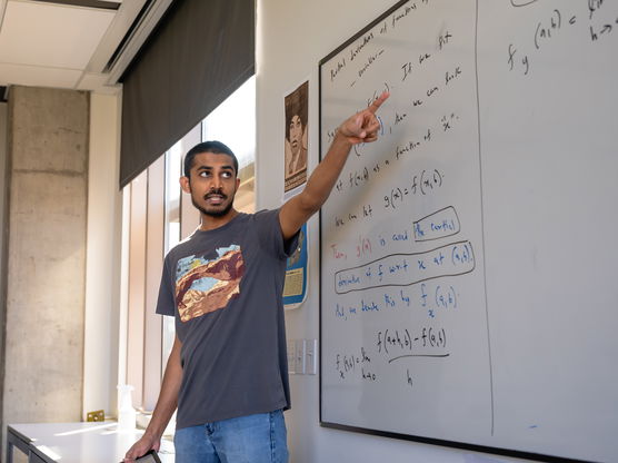 A student pointing to writing on a whiteboard in a classroom.