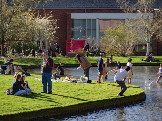 People enjoying sunshine on the grass surrounding Mill Stream in Salem