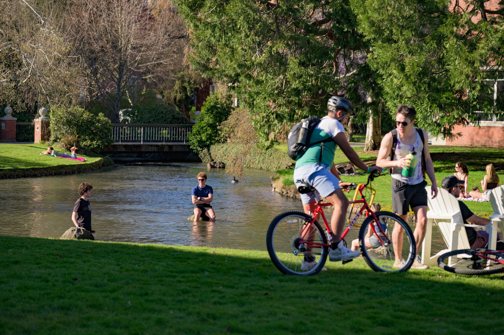 A group of Willamette students, one biking, some chatting on the grass, and others in the stream