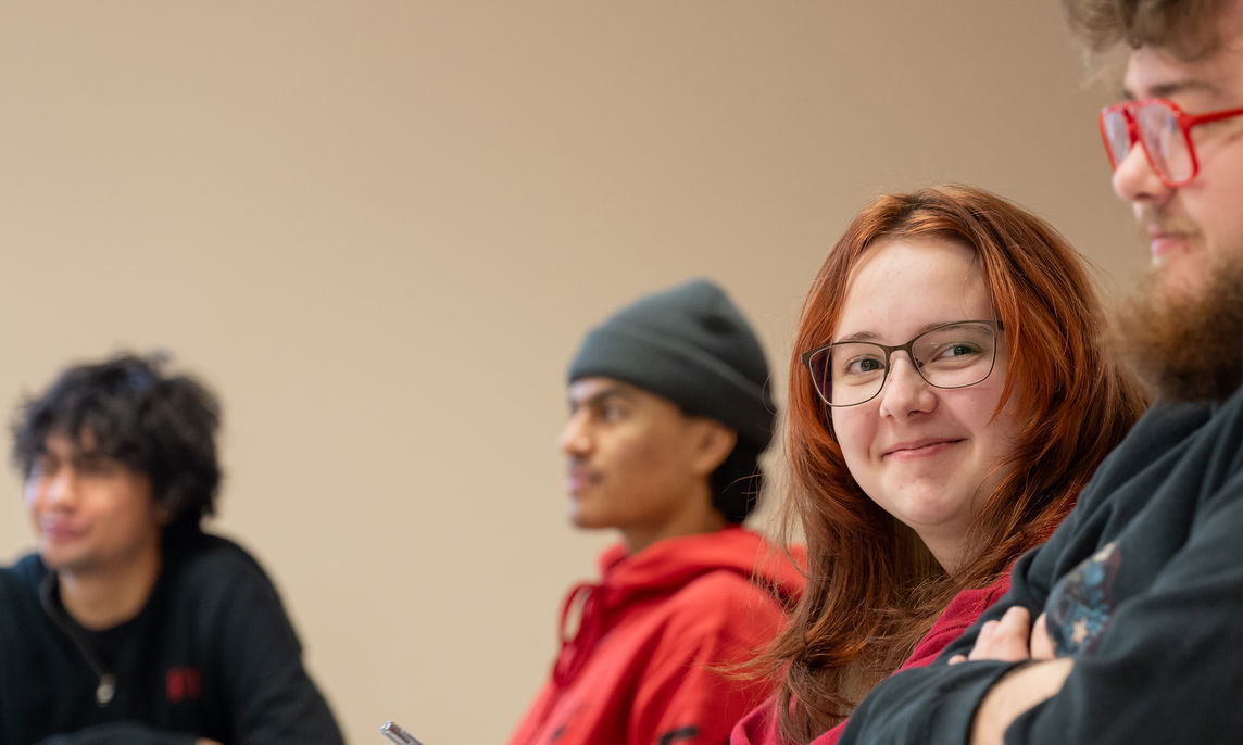 A student sitting and smiling with other students in a classroom. 