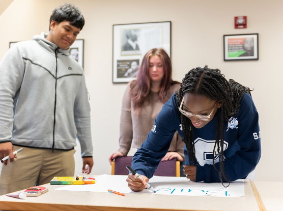 three students work on a project together with a large sheet of drafting paper in front of them