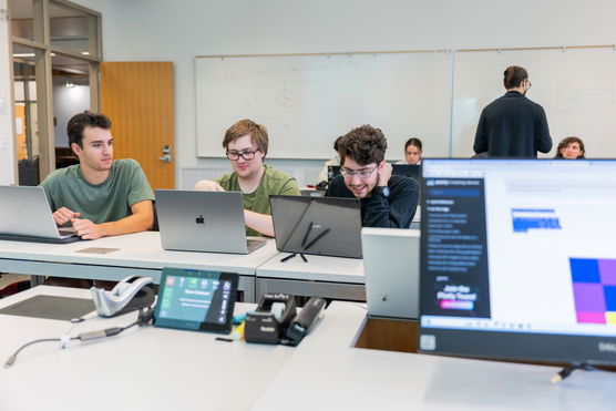 three students work happily on their laptops in a classroom