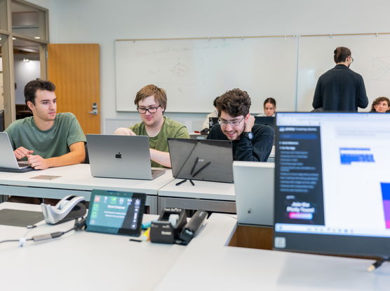 three students work happily on their laptops in a classroom