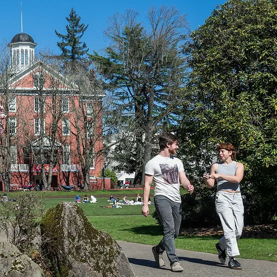 Two students walking with Waller Hall in the background at Willamette University's Salem campus