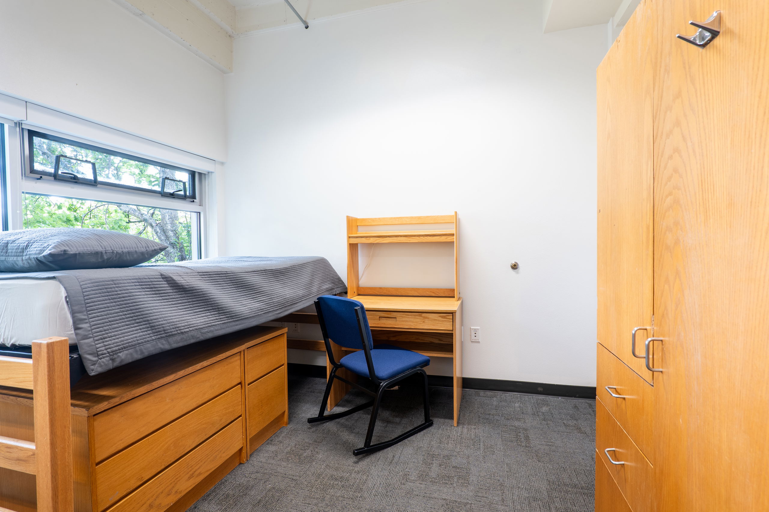 one side of a double room showing a bed, dresser, closet with drawers, desk, and chairs