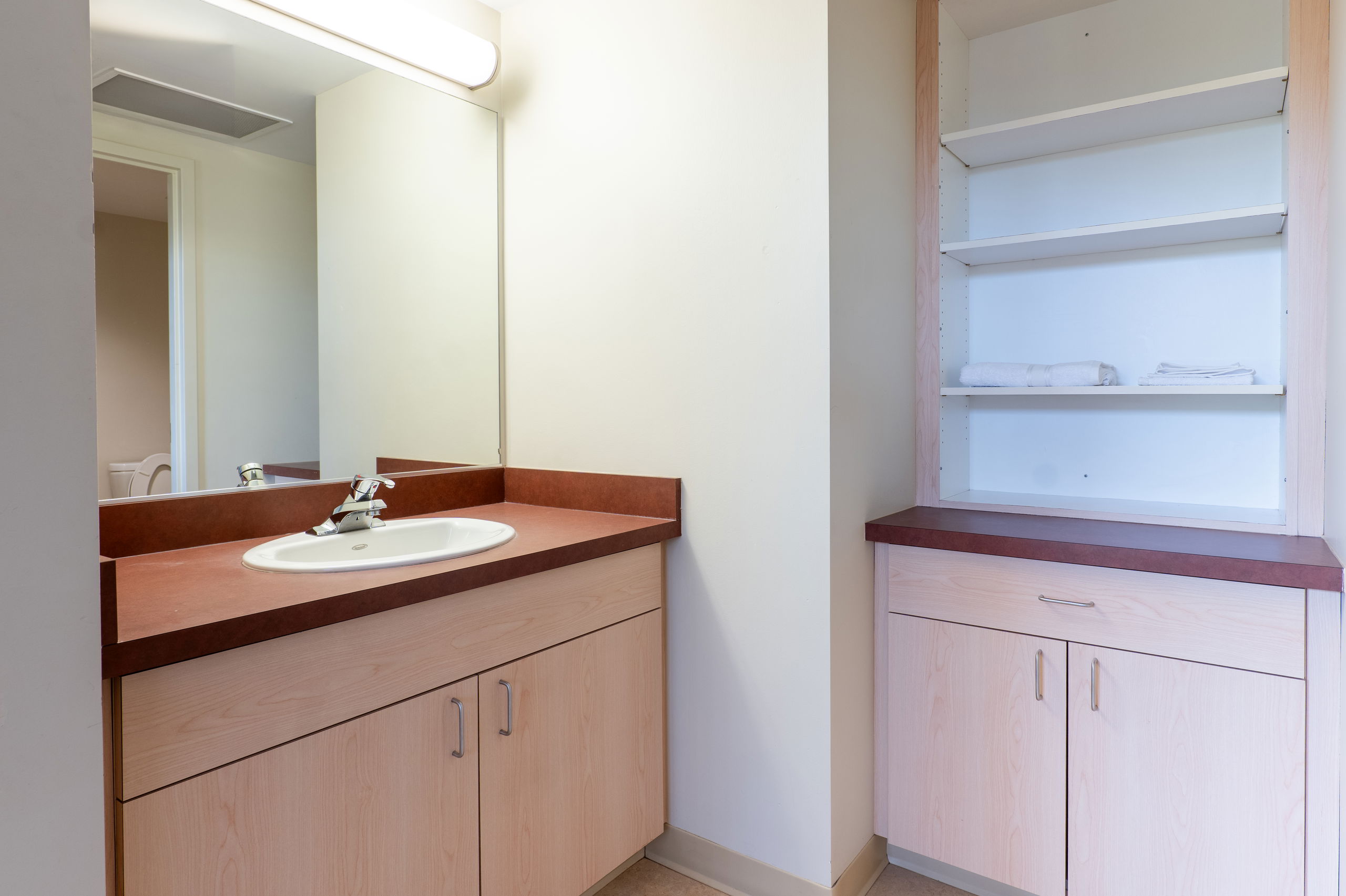 Apartment bathroom showing the sink and cabinet area with shelving for storage