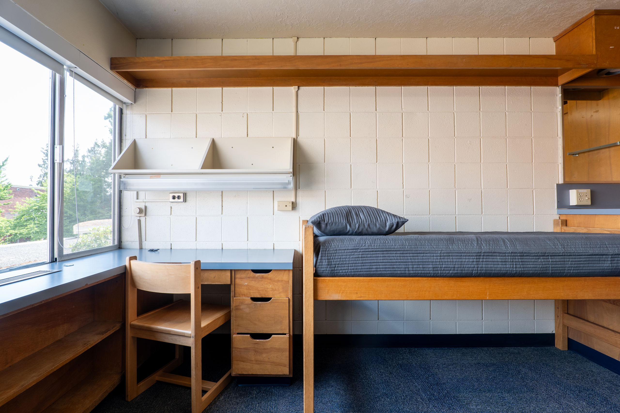 One side of a double room with a desk, bed, shelves, and chair