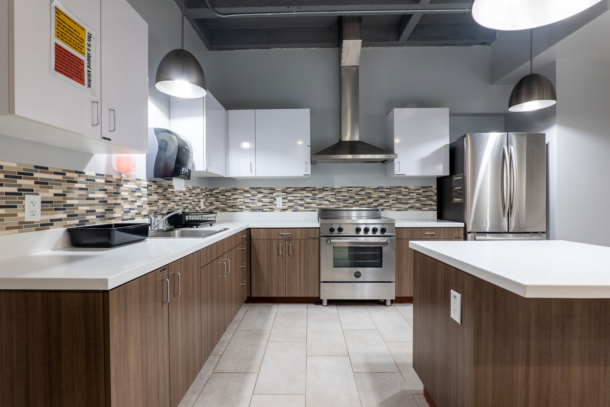 Communal kitchen showing middle island, fridge and freezer, oven and stove, and sink and counter area