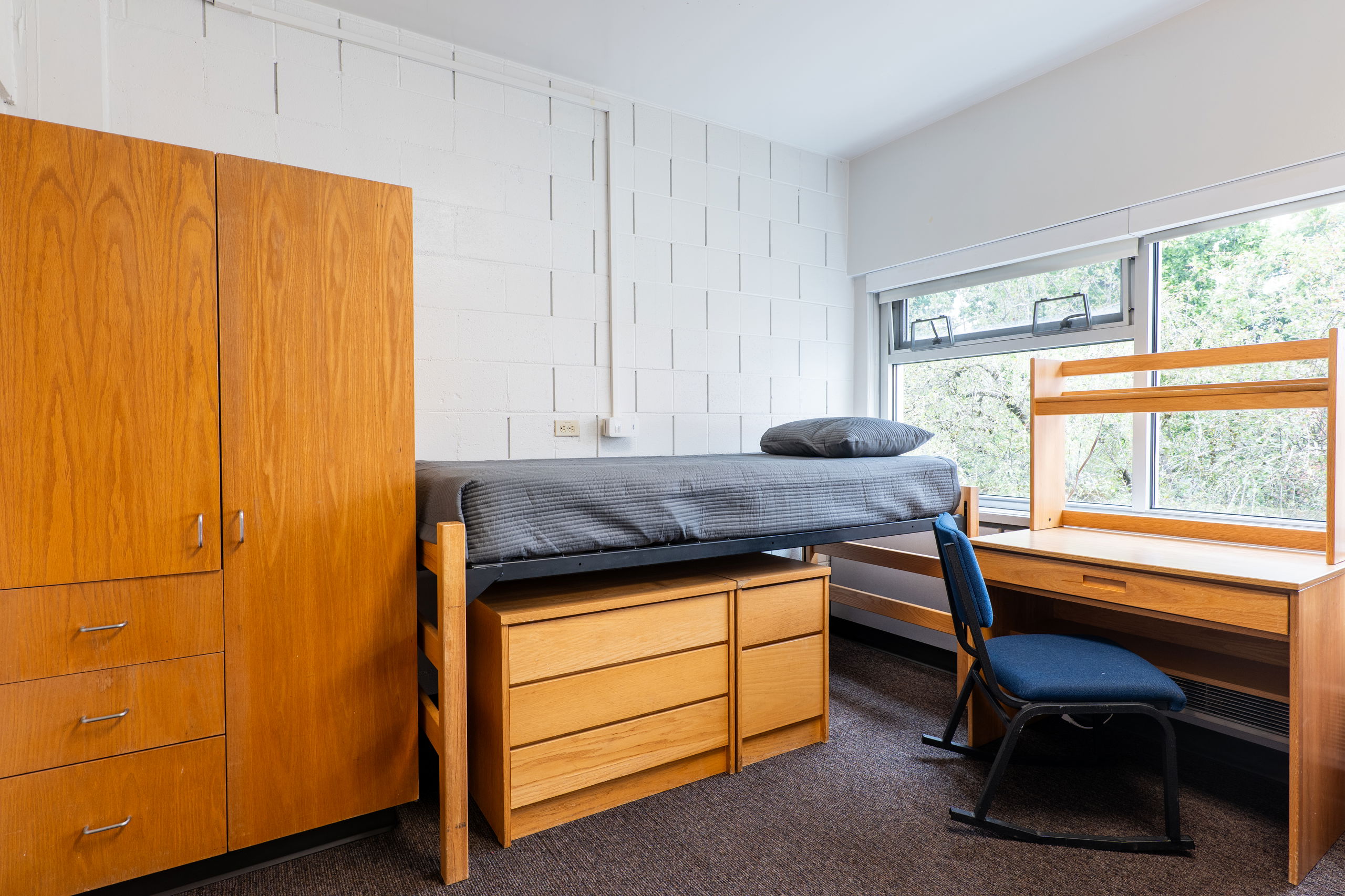 One side of a double room with a desk, bed, armoire, and chair