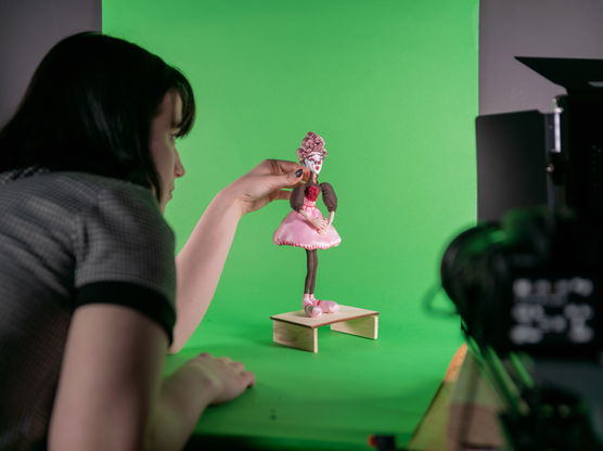 A PNCA student arranges a doll in a pink dress in front of a green screen