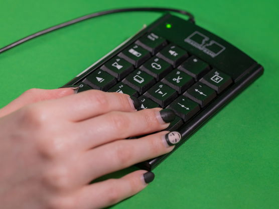 A hand with black fingernails holds a numerical keyboard on a green screen background