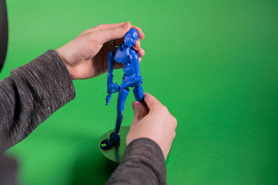 A PNCA student adjusts a blue plastic model of a human in front of a green screen in the Animated Arts lab