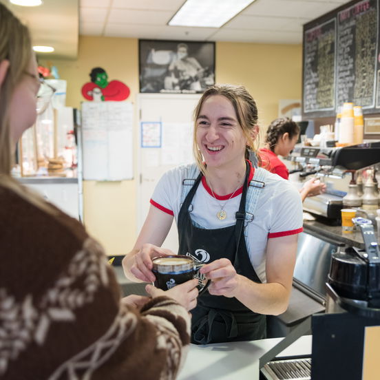 A student receives a mug of coffee from a barista behind the counter of Willamette Bistro