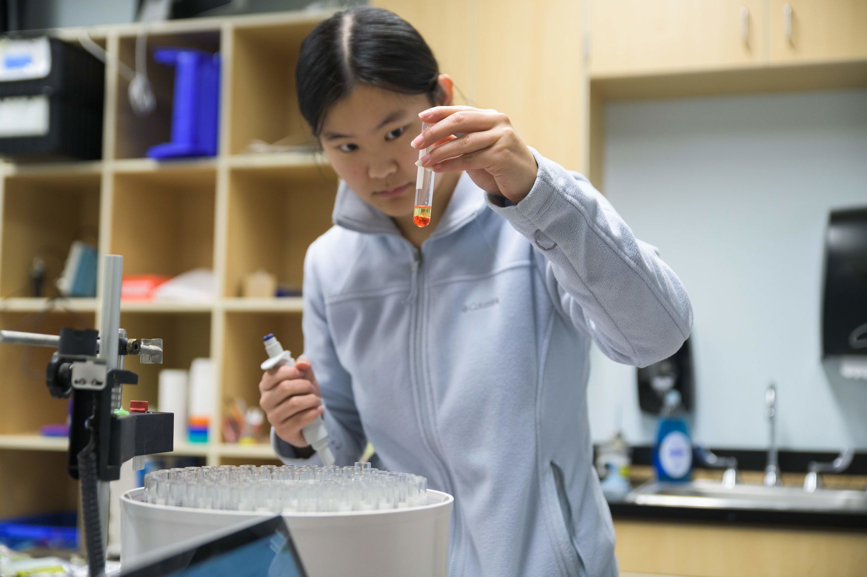 A Willamette student in a science classroom examines a test tube containing an orange liquid