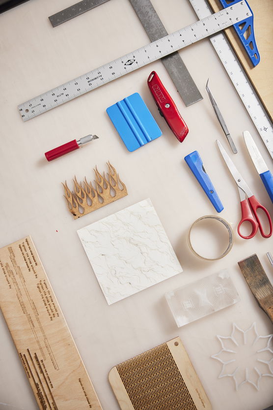 A collection of writing and drawing implements including various scissors, knives and rulers lay artfully arranged on a table