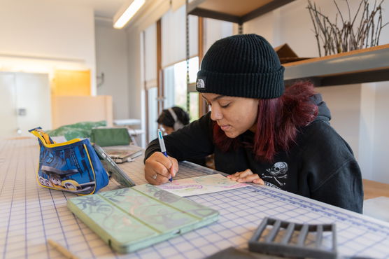 A PNCA undergrad student draws on a piece of paper on a gridded table in PNCA's 3-D Design classroom