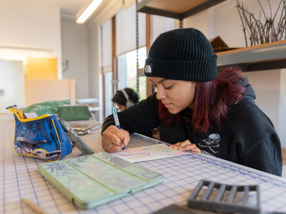 A PNCA undergrad student draws on a piece of paper on a gridded table in PNCA's 3-D Design classroom