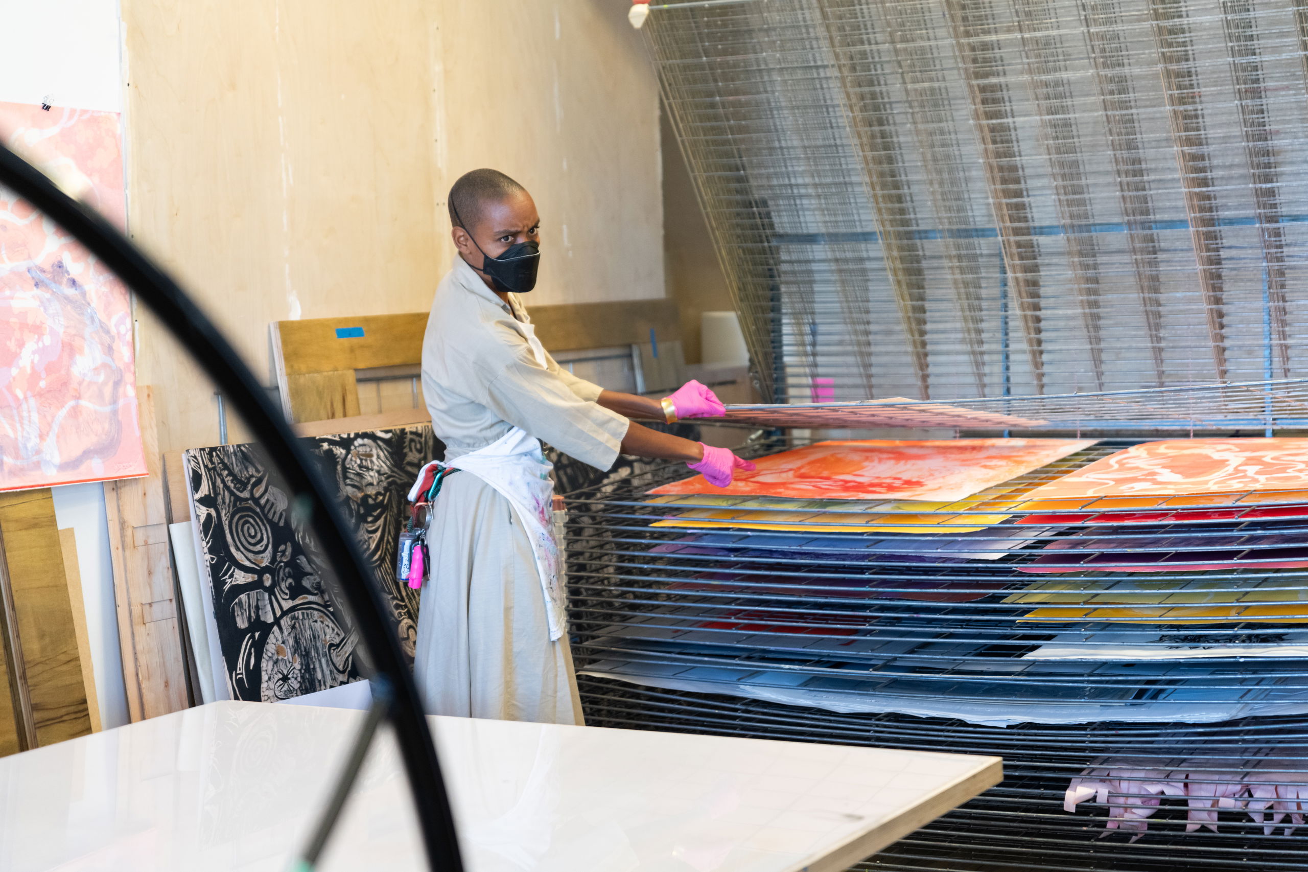 A PNCA professor wearing a face mask sorts through a stack of colorful prints in the printmaking studio