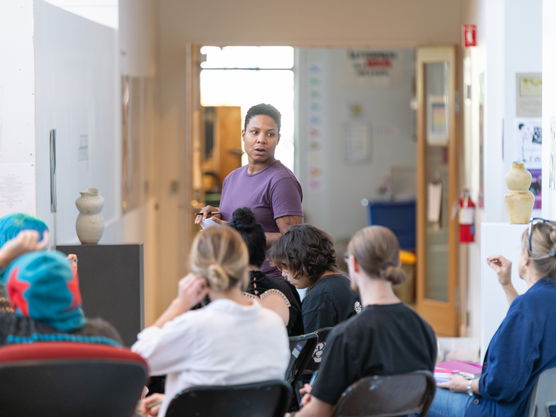 A PNCA instructor stands at the front of a class, leading a critique of a sculpture on a pedestal