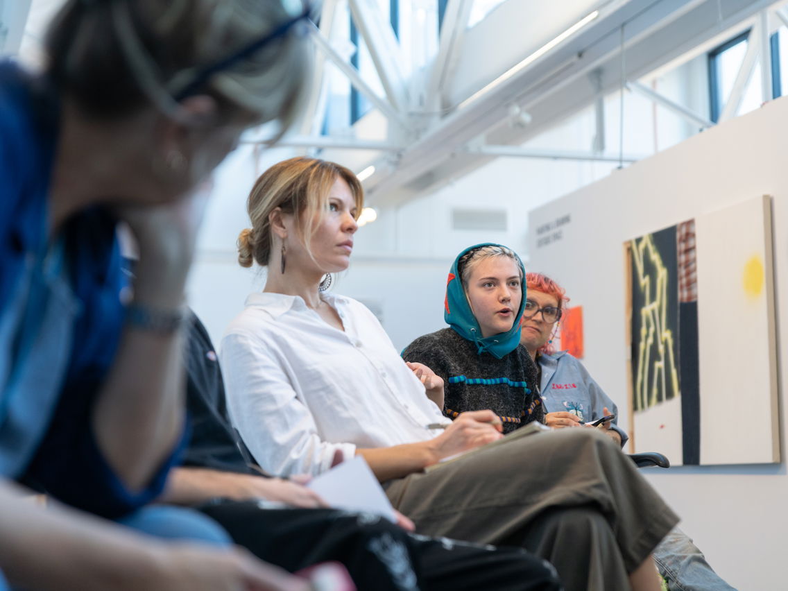 PNCA undergrad students sit in a line in an art gallery during a painting critique