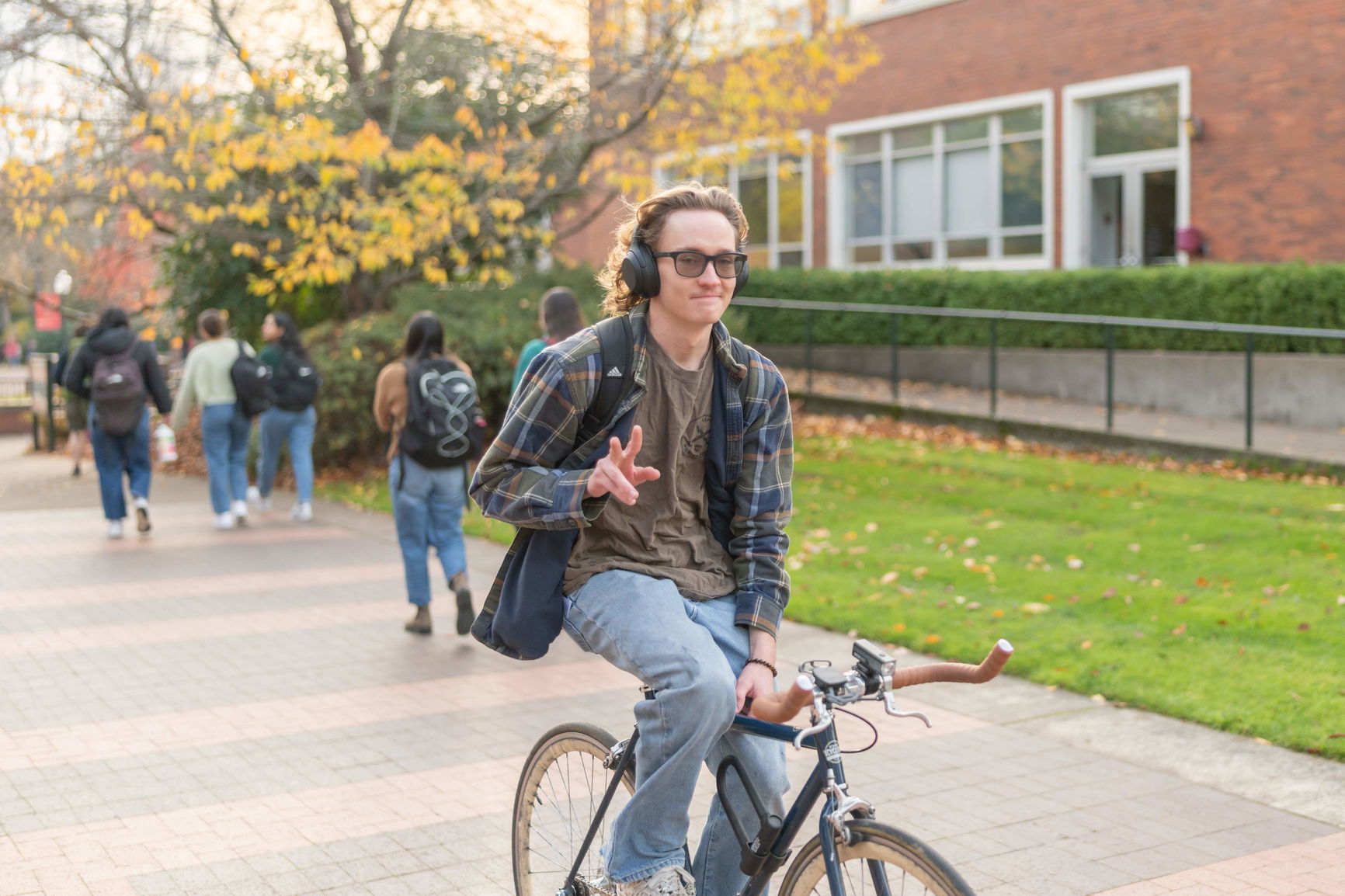 A waving student bikes across Willamette's campus in the fall as other students walk in the opposite direction