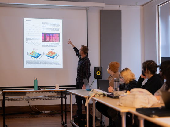 PNCA Professor Seth Nehil teaches a sound design class, gesturing to a graphic projected on a screen