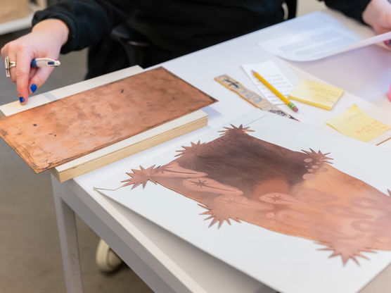 A PNCA student works at a table with papers, pencils and stencils