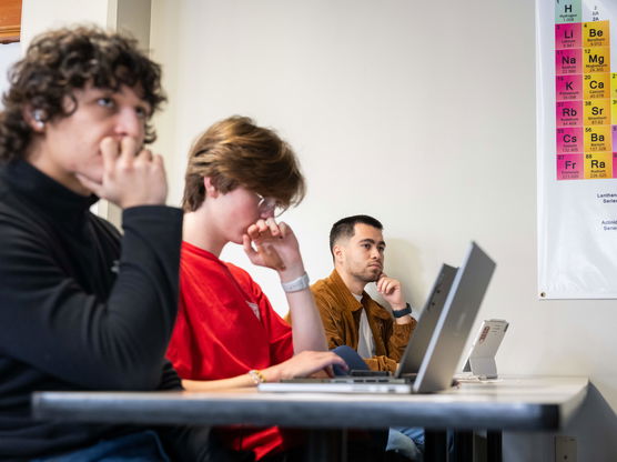 Willamette data science students sit at a table with their laptops and listen to a lecture