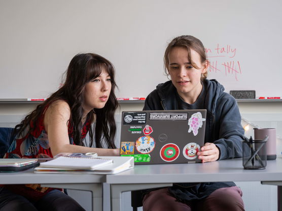 Two Willamette students in a classroom work together on a laptop covered in stickers