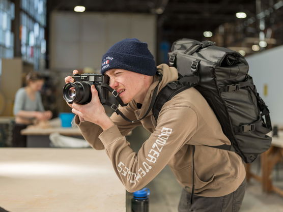 A PNCA BFA student wearing a beanie and carrying a backpack takes photos in the ceramics studio