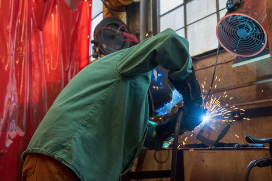 A PNCA student wearing a mask in the woodworking studio cuts metal while sparks fly