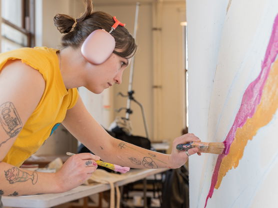 A PNCA student paints a pink and yellow streak down a large canvas during a mural painting class