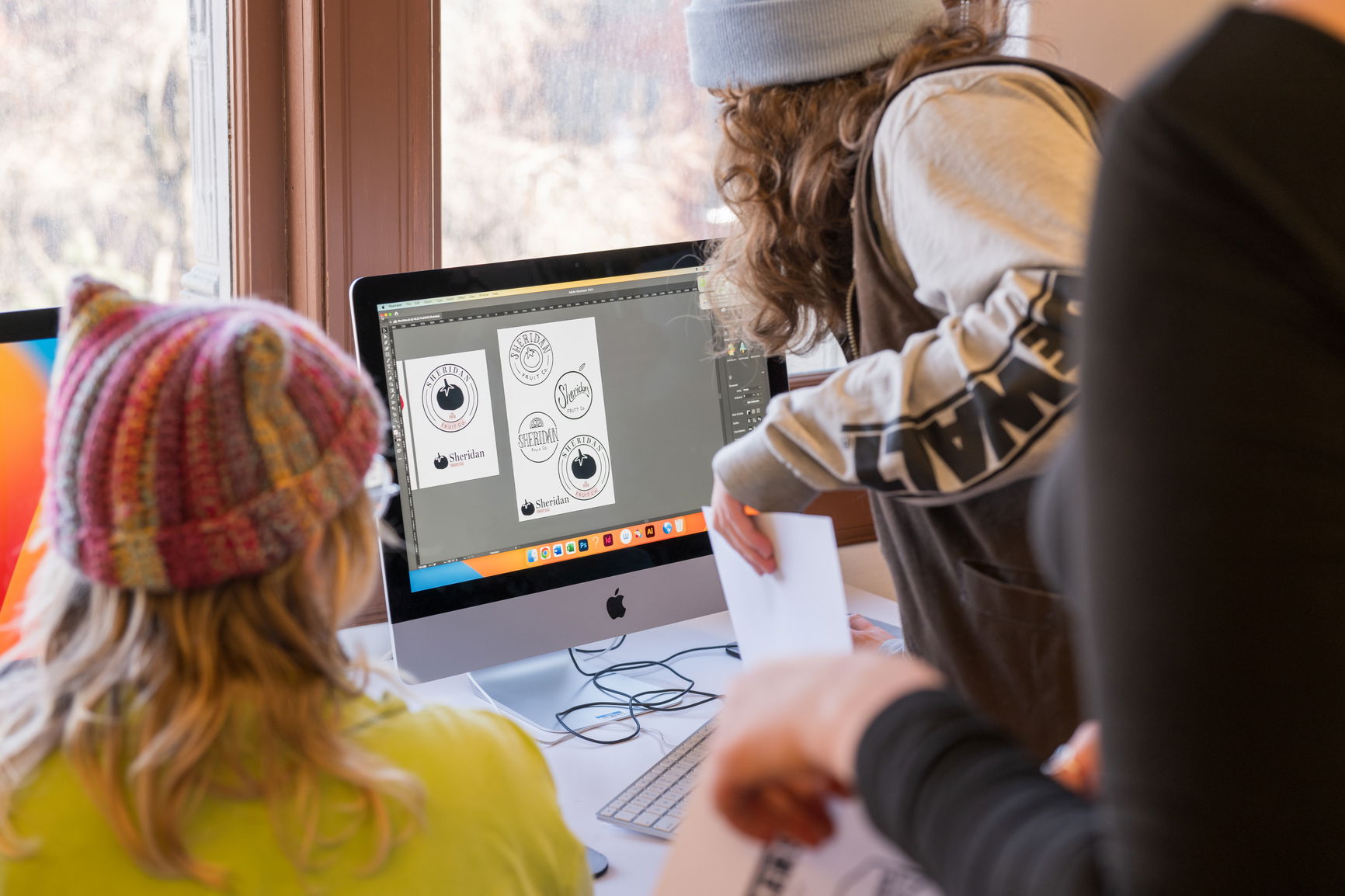 PNCA graphic design students lean over a computer monitor displaying logo illustrations